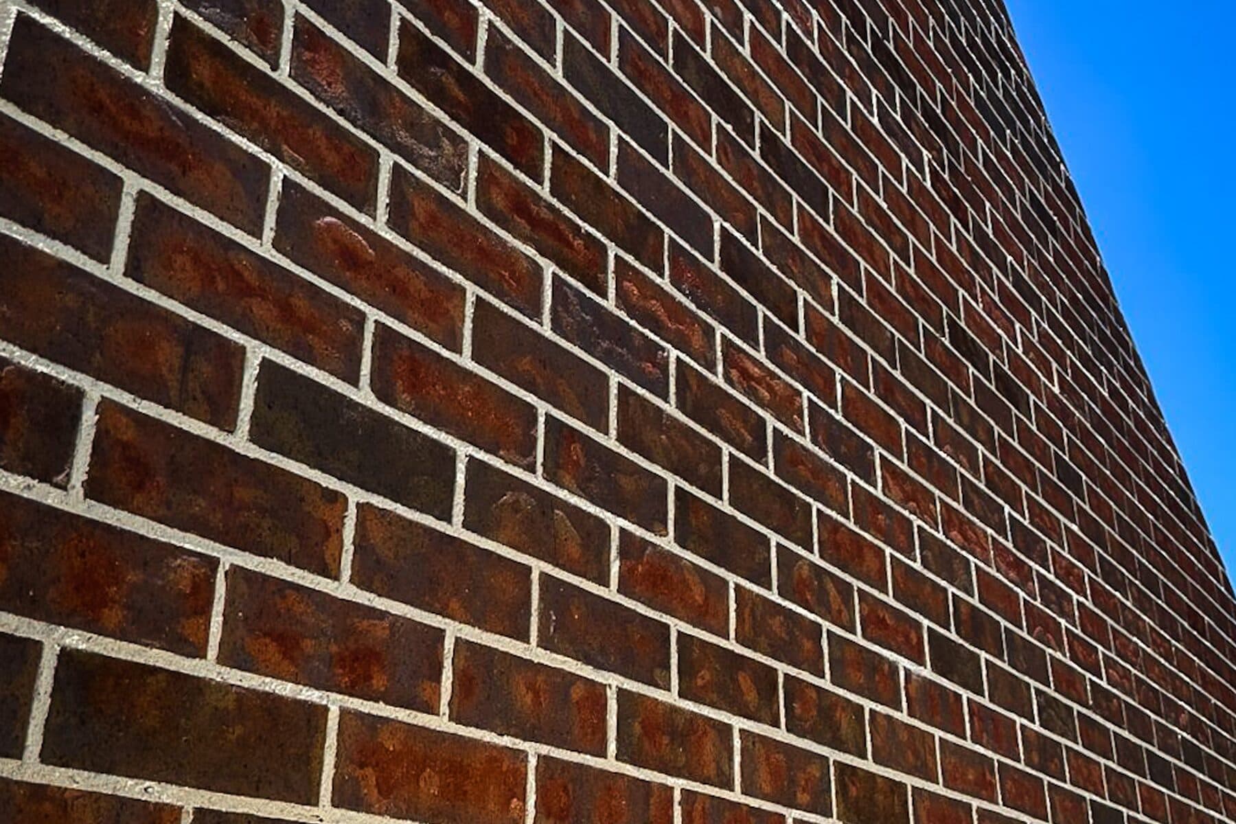 Raking close-up of red brindle face brickwork against a clear sky