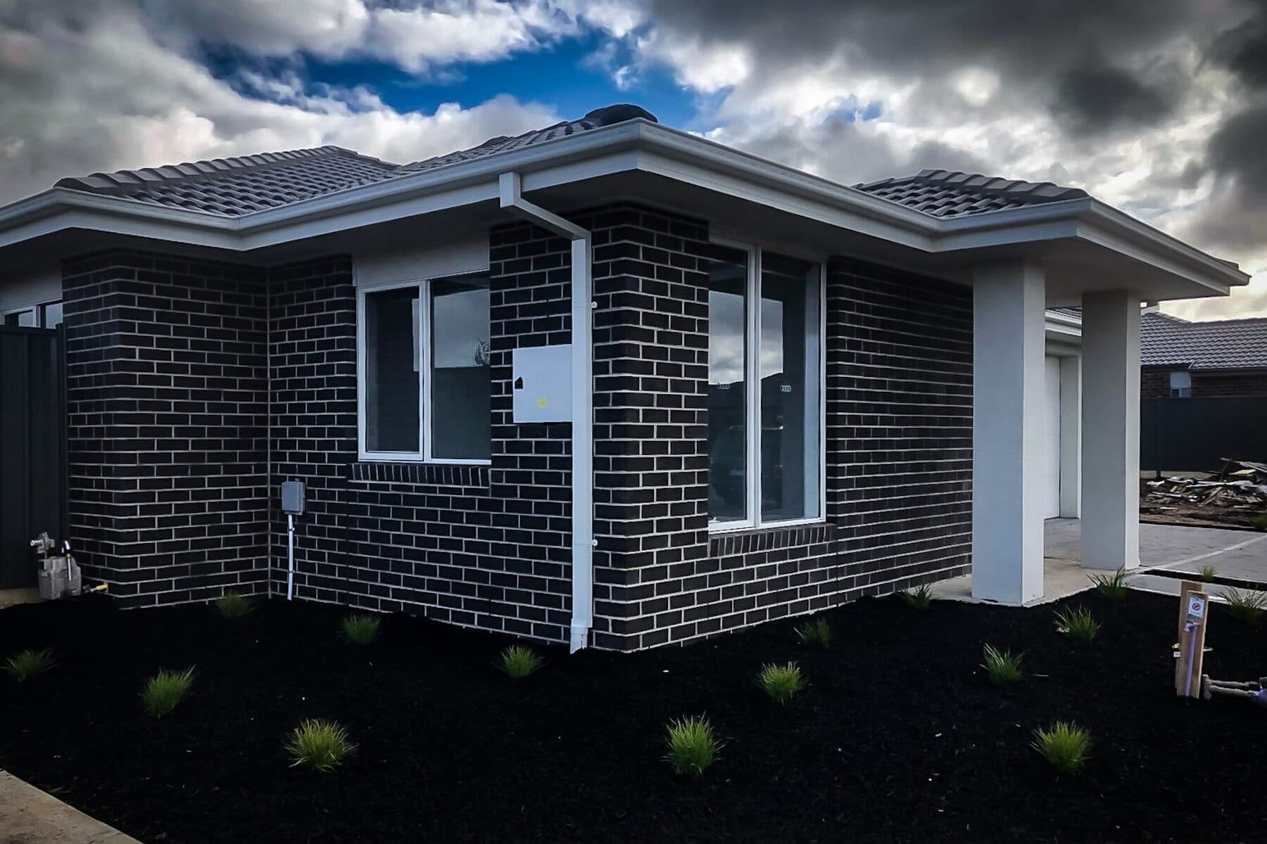 Corner of a new single-storey home in charcoal face brick with rendered posts