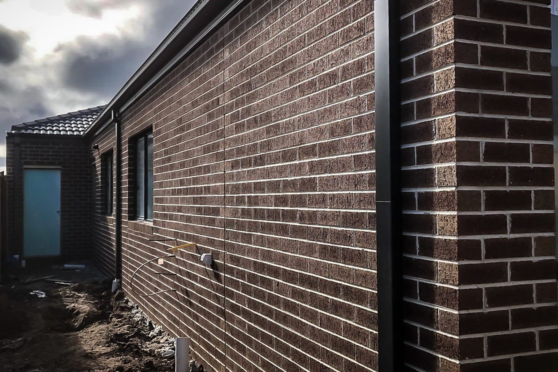 Raking view along a red brindle face brick wall under a heavy sky