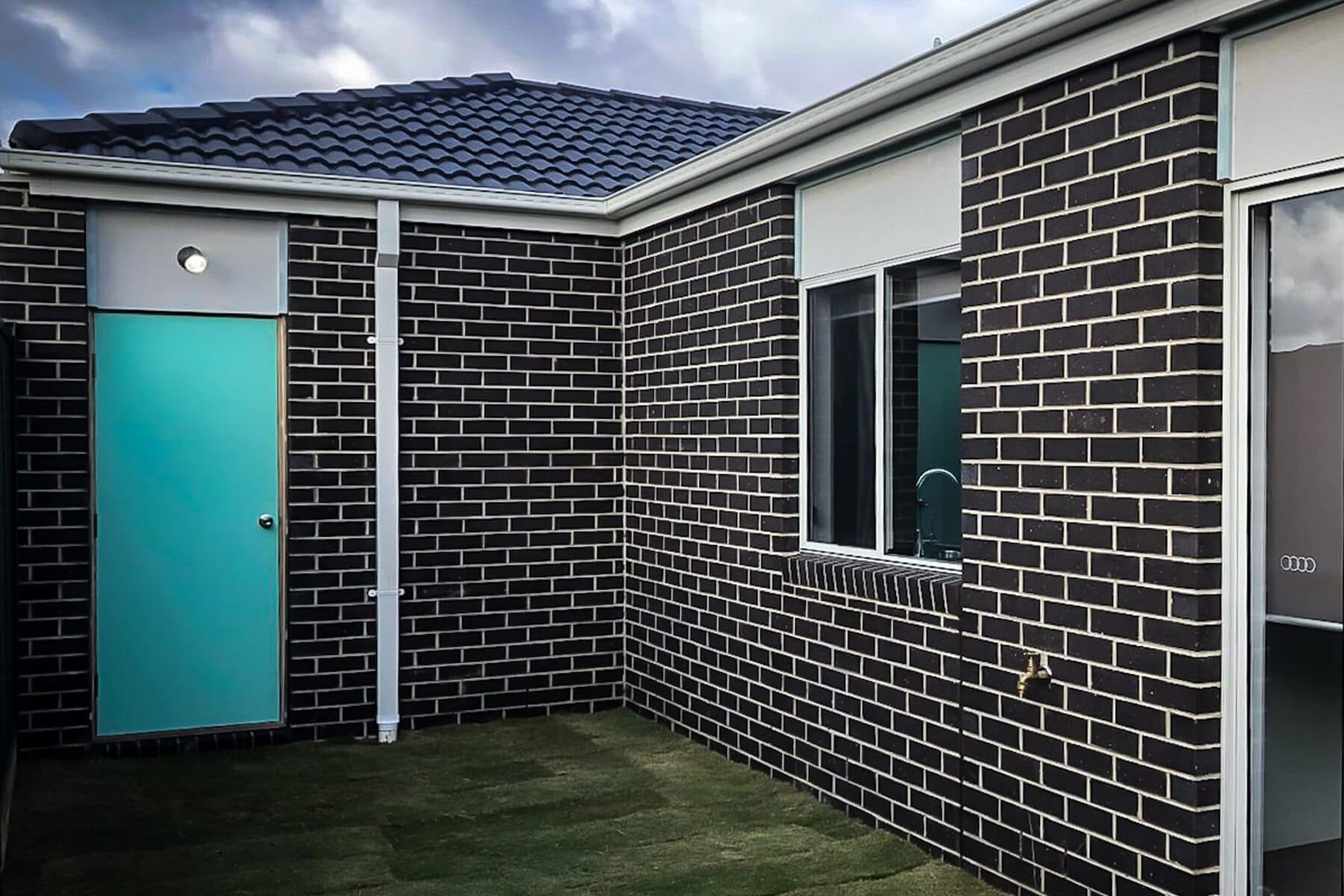 Charcoal brick courtyard with a teal entry door and fresh turf