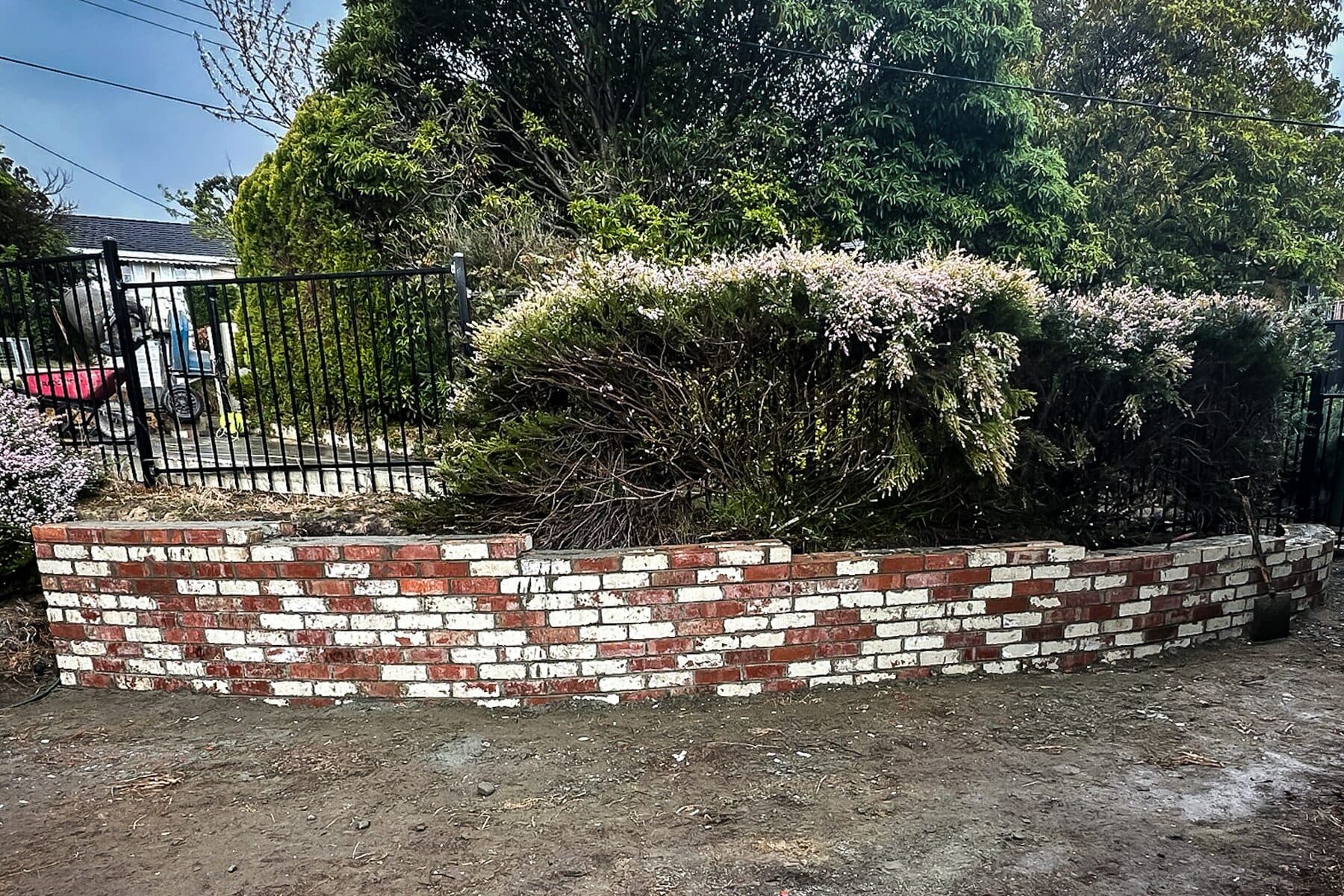 Low curved garden wall in reclaimed red brick behind a steel fence